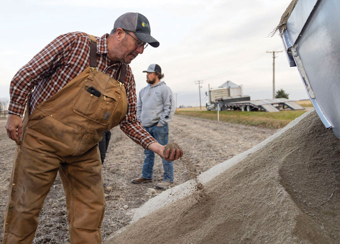 A farmer inspects rock dust while another farmer looks off into the distance