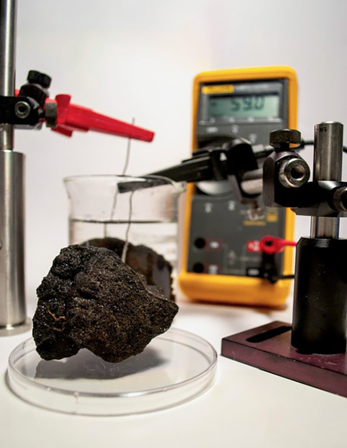 A metal claw reaches for a round nodule on the seafloor.